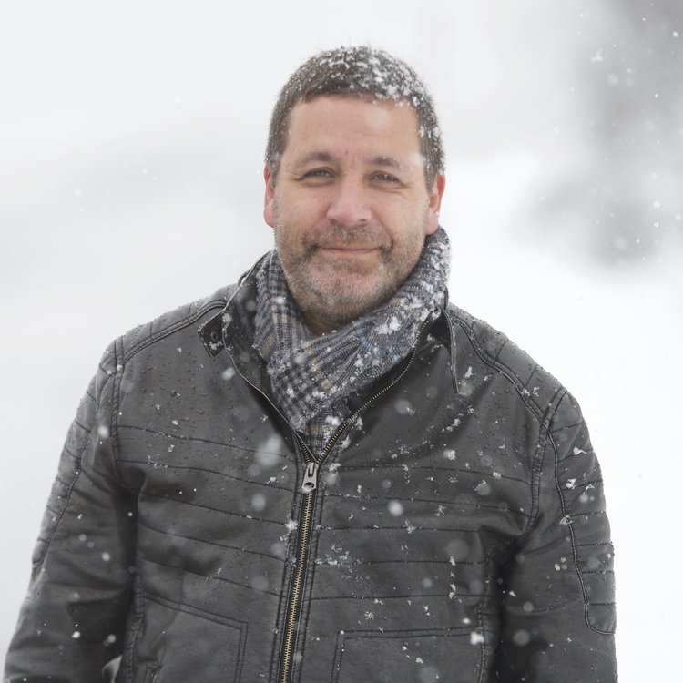 Smiling man in snowfall, wearing jacket and scarf, winter portrait.