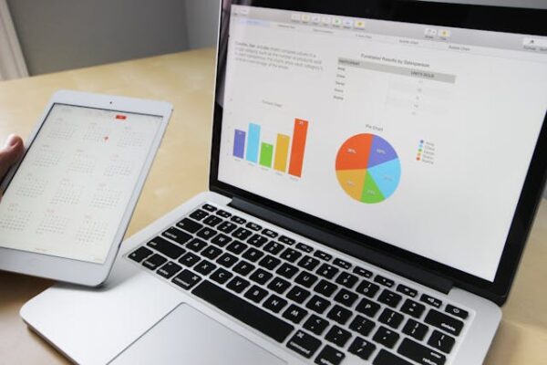 Modern laptop and tablet on desk, displaying colorful graphs for business analysis.