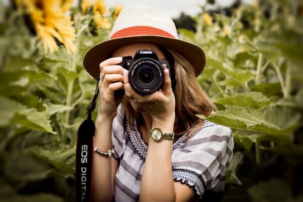 Stylish photographer with camera in nature, wearing hat, stripes, watch.